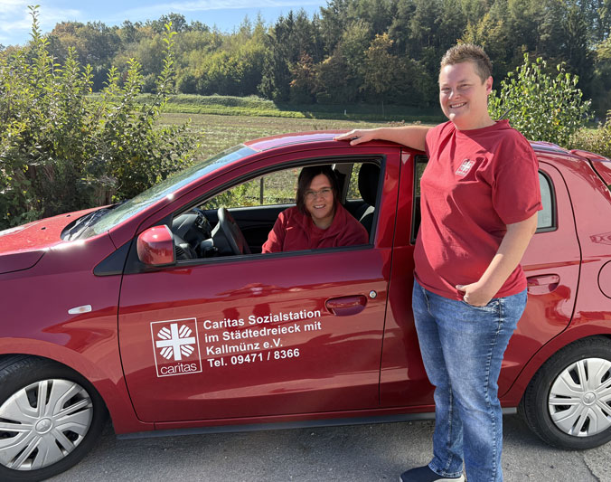 caritas-team-teublitz-2 Zwei lächelnde Pflegekräfte der Caritas im Einsatzfahrzeug für die ambulante Pflege im Städtedreieck.